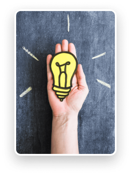 A hand holding a paper light bulb against a chalkboard